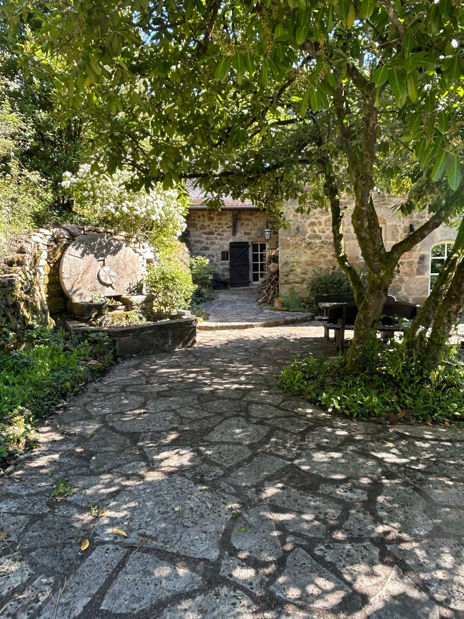 Cour pavée ombragée du moulin menant à l'entrée du gîte